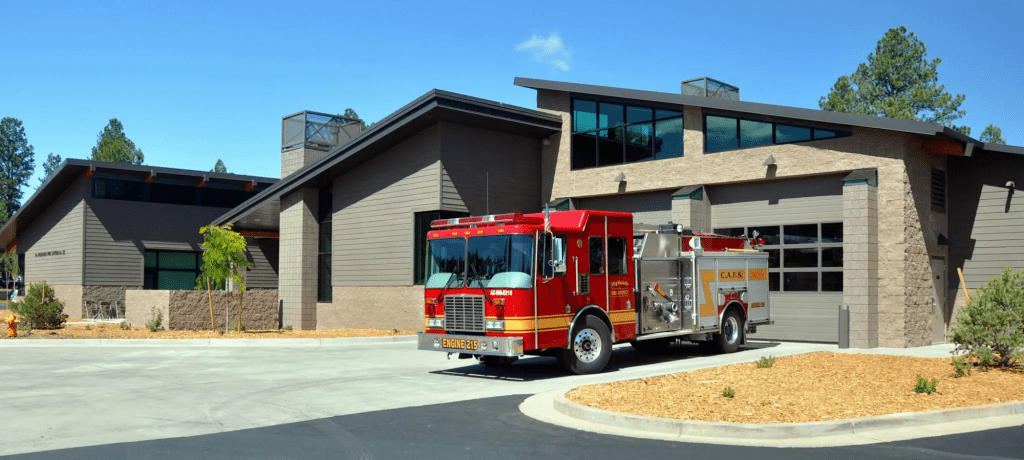 A red fire truck is parked in front of the modern Highlands Fire Station No. 23, which recently received the Coconino County Advanced Award for Sustainability, under a clear blue sky.