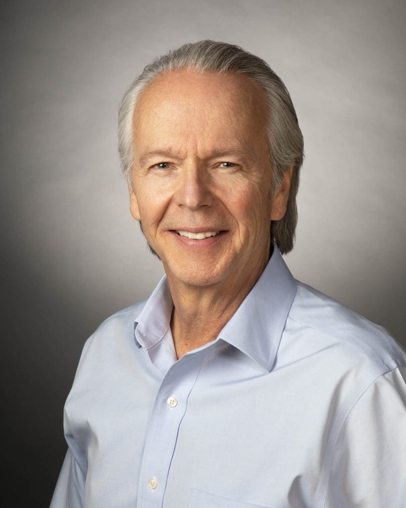 Kinney President Tim Kinney, smiling in a light blue collared shirt, is posed against a plain gray background as he speaks with 12 News about Kinney's commitment to United Way of Northern Arizona.
