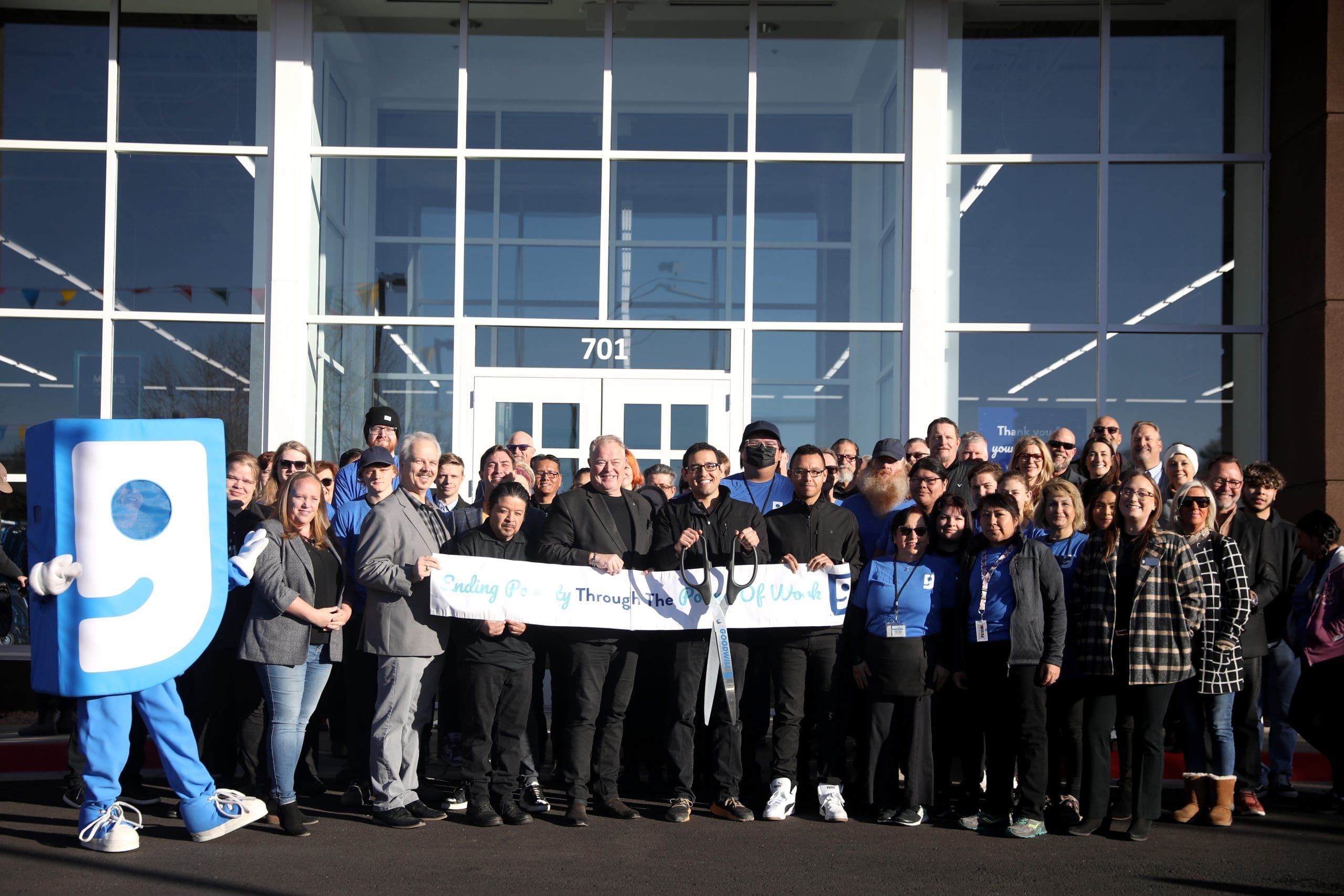 A group of people, including a mascot, stand in front of a building holding a ribbon for a ribbon-cutting ceremony, celebrating “Building Better Together for a Greener Tomorrow: How Kinney Honors Earth Day.”.