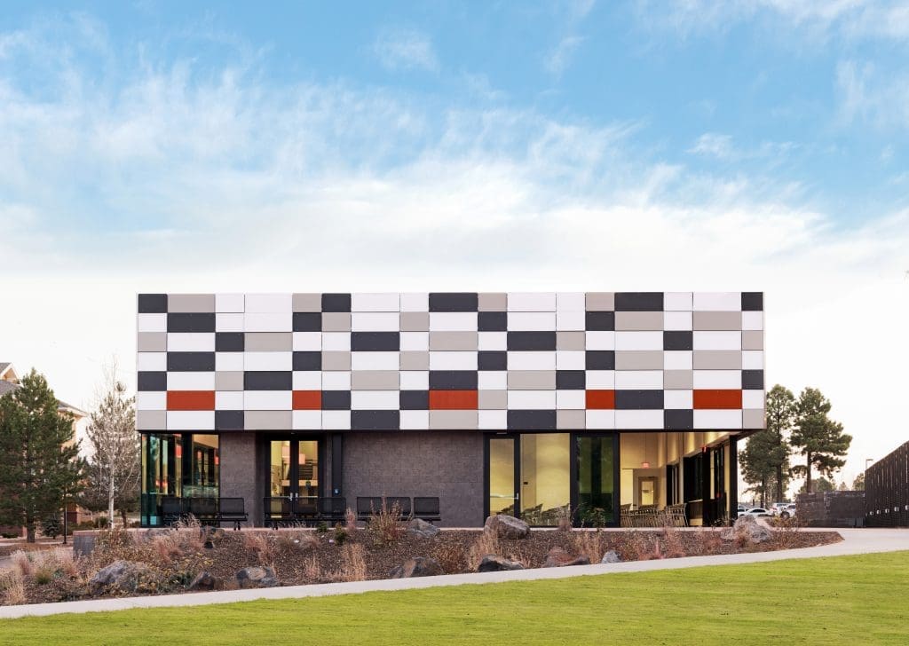 Modern building with a rectangular design and checkered facade of black, white, and gray panels, large windows, and a landscaped lawn—showcasing how Kinney is Building Better Together for a Greener Tomorrow in honor of Earth Day.