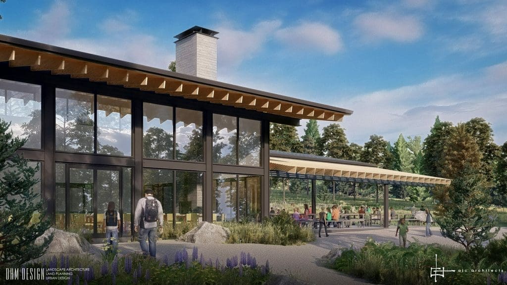 A modern building with large glass windows stands amid greenery, with people walking outside and others seated at outdoor tables under a covered patio.