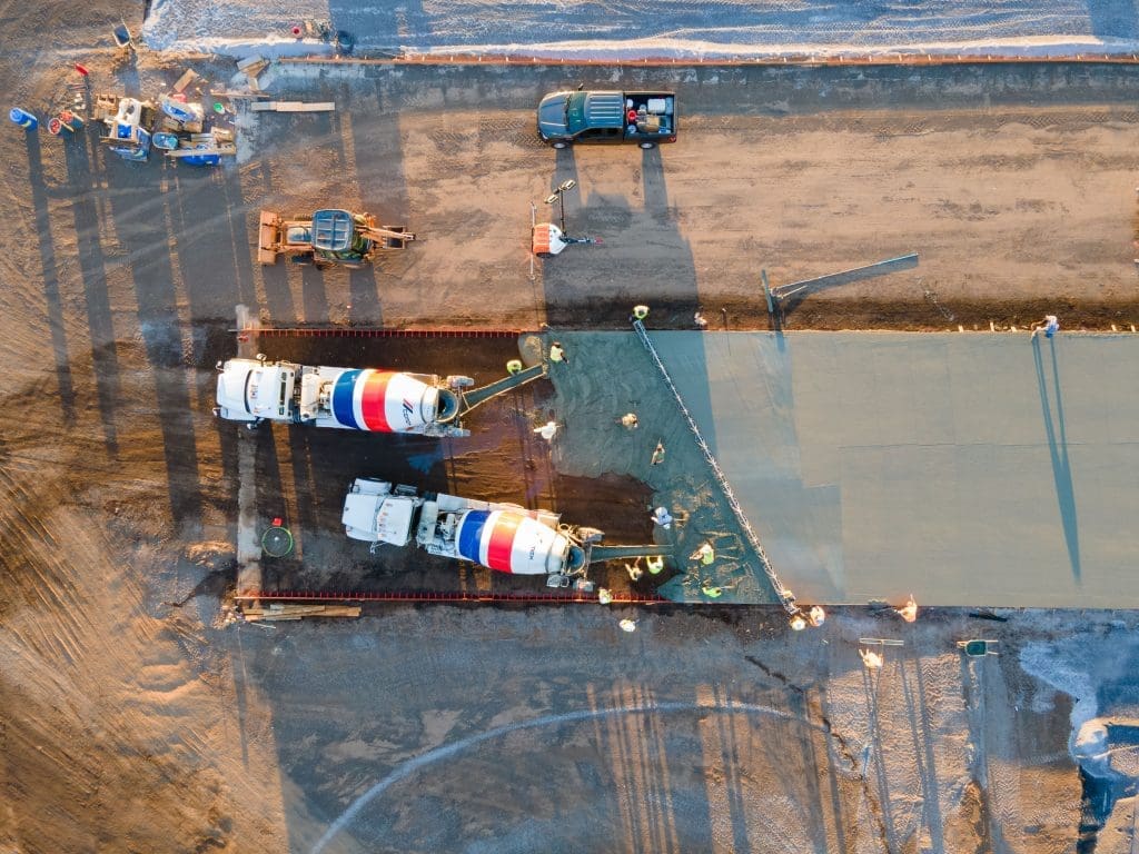 Aerial view of construction workers shaping concrete pavement with two cement trucks on a large site, showcasing rewarding careers in construction.
