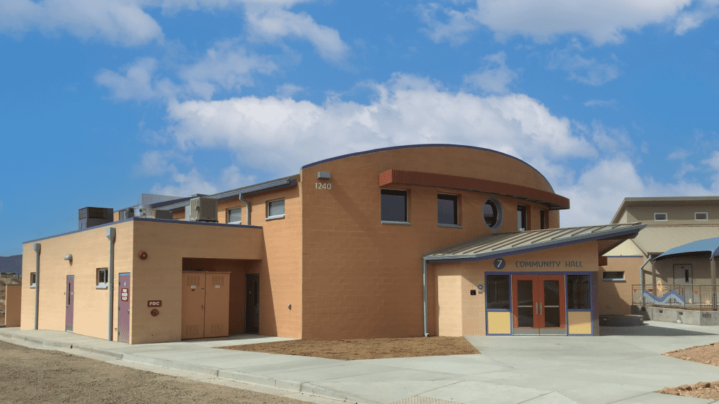 A modern, tan-colored community hall building with angular and curved features, set against a blue sky with scattered clouds.