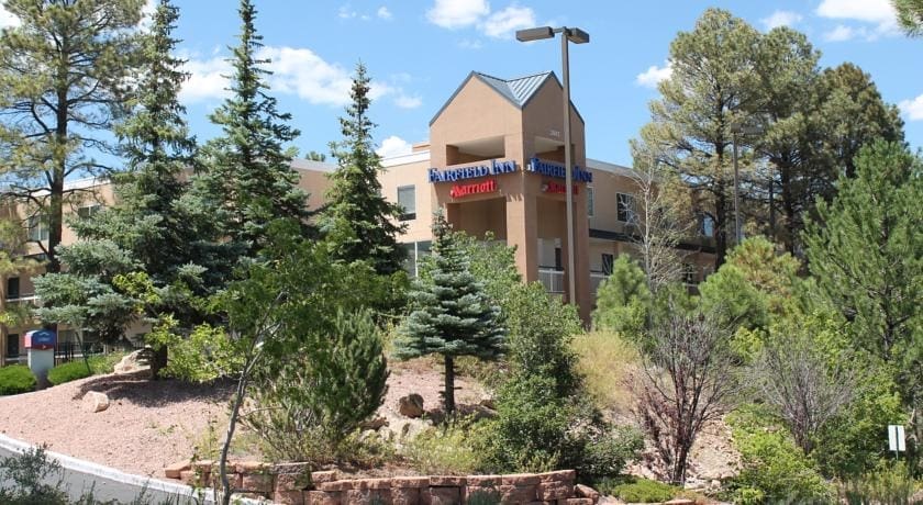A Fairfield Inn & Suites by Marriott hotel building surrounded by trees and shrubs under a partly cloudy sky.