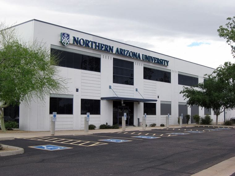 A white, two-story building with a sign reading "Northern Arizona University" above the entrance, surrounded by a parking lot with several accessible parking spaces.