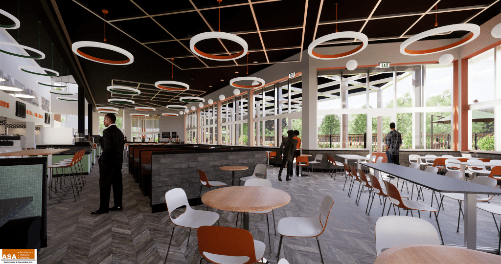 Modern cafeteria interior with round light fixtures, wooden tables, and white chairs. Several people are standing and sitting near large windows with views of greenery outside.