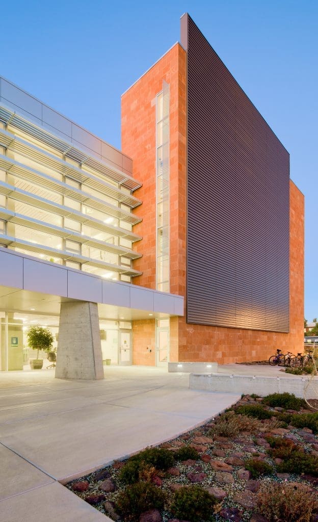 Modern building with glass and metal facade, red stone wall, and landscaped area in front, photographed at dusk—the Northern Arizona University Extended Campuses Facility stands out with contemporary design.