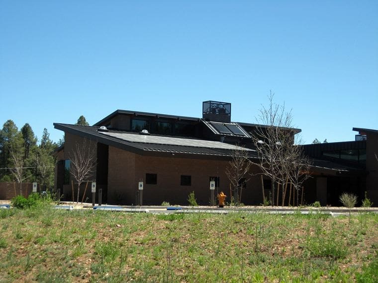 A modern building with a sloped roof, brick exterior, and Highlands Fire District PV System solar panels stands amid a grassy area with young trees under a clear sky.