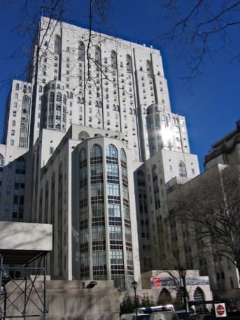 Tall, white Art Deco style hospital building with many windows, set against a clear blue sky with some bare tree branches visible.