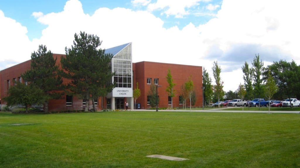 A red brick building labeled "University Union" stands behind a large green lawn, with trees and parked cars visible nearby under a partly cloudy sky.