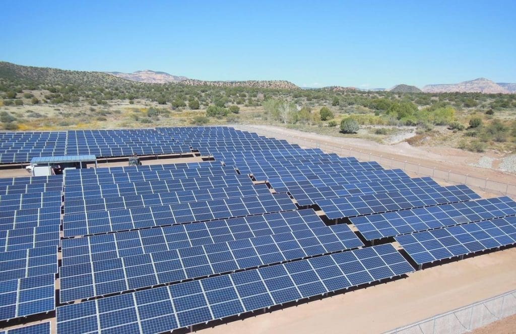 Rows of solar panels are installed on a large plot of land in a sunny, arid landscape near the Sedona Wastewater Reclamation Plant PV System, with hills and trees in the background.