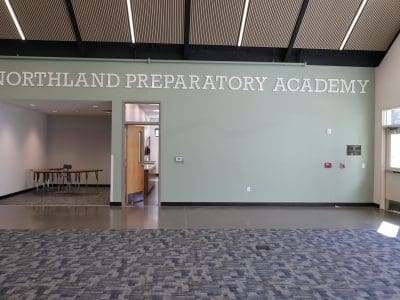 Interior view of the Northland Preparatory Academy STEAM Building hallway, featuring "Northland Preparatory Academy" on the wall, an open classroom door, and large windows letting in abundant natural light.