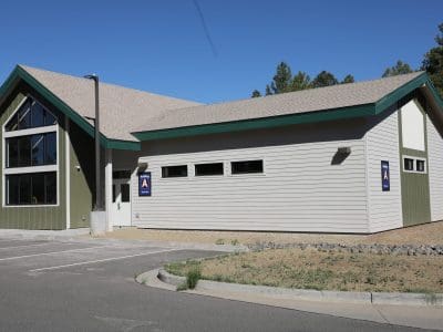 Single-story Northland Preparatory Academy STEAM Building with large windows, green trim, and two handicap parking signs on the wall, adjacent to an empty parking lot under a clear sky.