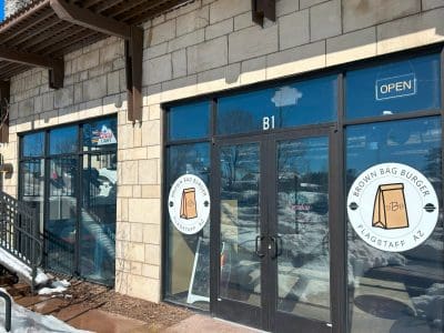 Exterior view of Brown Bag Burger restaurant in Flagstaff, Arizona, with glass doors, signage, and snow on the ground outside.