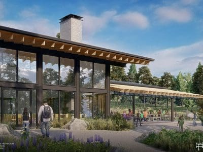 Modern building with large windows and outdoor seating area surrounded by greenery, featuring the Camp Colton Lodge PV System; people are walking and sitting under a partly cloudy sky.