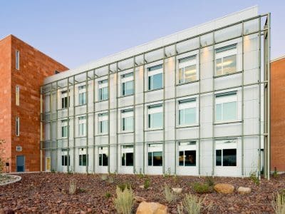 Modern three-story Northern Arizona University Extended Campuses Facility featuring a grid-like facade, large windows, and a desert landscaped front with rocks and sparse vegetation.