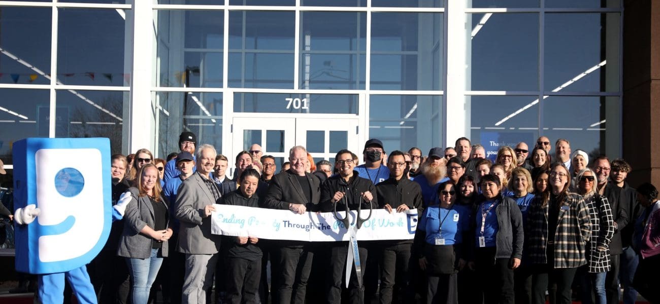 Goodwill A group of people, including a mascot, stand in front of a building holding a ribbon for a ribbon-cutting ceremony, celebrating “Building Better Together for a Greener Tomorrow: How Kinney Honors Earth Day.”.