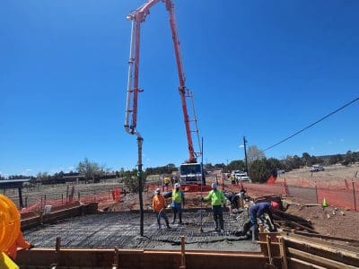 Construction workers pour and level concrete at a building site with a large concrete pump truck under a clear blue sky.