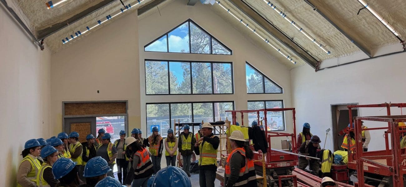 NPA NAU Interior Design Tour 2 Inspiring the Next Generation: Interior Design Students visit a Kinney job site, where they gather in construction vests and hard hats inside a partially finished building with exposed ceiling insulation and large windows.