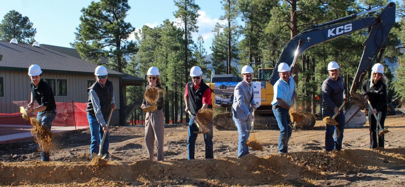 NPA STEAM Building Groungbreaking Ceremony Seven people wearing hard hats use shovels to break ground at the Northland Preparatory Academy STEAM Building Groundbreaking Ceremony, with an excavator and trees in the background.