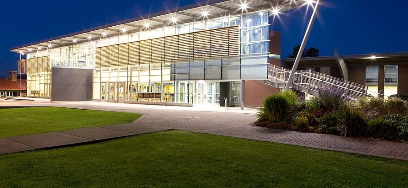 National Estimating Award Modern building with large glass windows and a metal overhang, illuminated at night, with a lawn and landscaped area in the foreground—showcasing Kinney’s commitment to Building Better Together for a Greener Tomorrow.