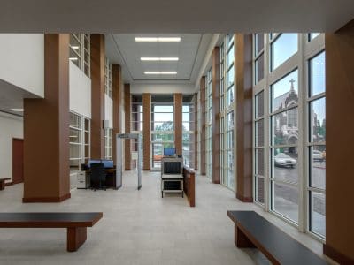 A spacious room with high ceilings, tall windows, benches, an empty desk, and a security checkpoint near the entrance.