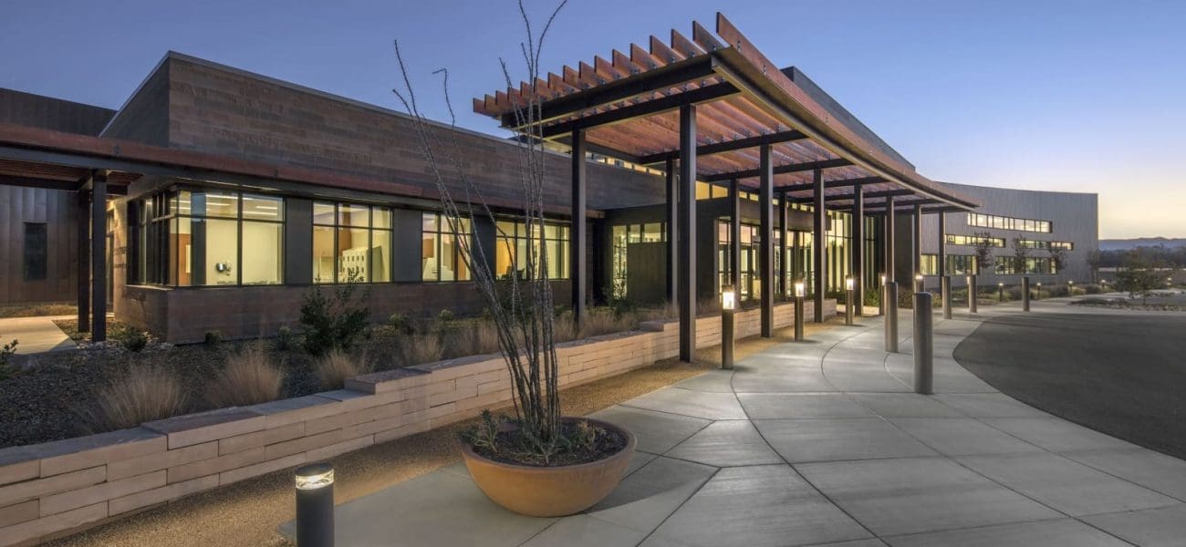 Modern building with large windows and a covered walkway at dusk, surrounded by landscaped planters and exterior lighting, as seen at Verde Valley Medical Center – Camp Verde Campus, recipient of Arizona Masonry Guild’s Excellence in Masonry Architectural Award.