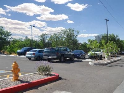Parking lot with several cars parked, a yellow fire hydrant in the foreground, and trees and blue sky with clouds in the background.