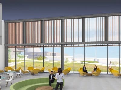 Spacious modern lobby with large windows, yellow chairs, white tables, and several people sitting or conversing in a well-lit, open area.