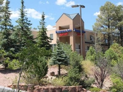 A Fairfield Inn & Suites by Marriott hotel building surrounded by trees and shrubs under a partly cloudy sky.