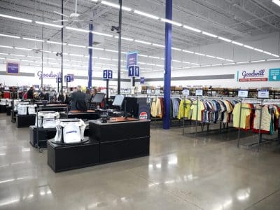 Interior of a Goodwill thrift store showing checkout counters, clothing racks, and overhead signs in a well-lit, spacious area.