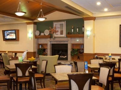 A dining area with several tables and chairs, a fireplace, framed art on the walls, a TV, and overhead lighting.