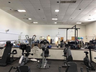 A gym with various exercise machines, including stationary bikes and ellipticals, with mirrors and fitness equipment visible in the background.