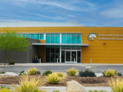 A modern medical building with a sign that reads "Ironwood Cancer & Research Centers" on a yellow and gray exterior, landscaped with desert plants.
