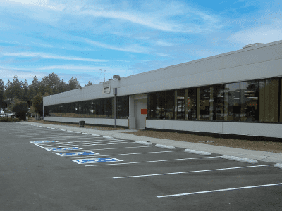 Single-story office building with large windows and multiple empty accessible parking spaces in front under a blue sky.