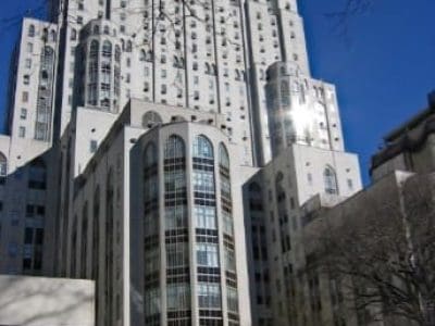 Tall, white Art Deco style hospital building with many windows, set against a clear blue sky with some bare tree branches visible.