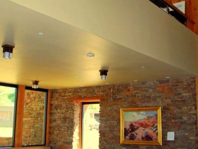 Modern interior room with stone walls, large windows, concrete floor, and a landscape painting hanging on the wall beneath an open upper level.