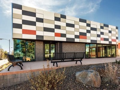Modern building with a checkerboard-patterned facade in black, white, and red tones, large windows, benches, and landscaped area with rocks and plants in front.