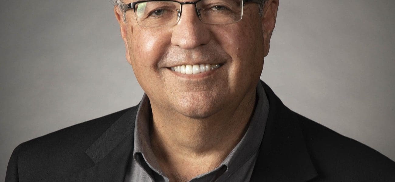 rich formal Rich Bowen, a middle-aged man with glasses, gray hair, and a gray shirt under a black blazer, smiles at the camera against a plain background. He is a proud NACET Moonshot Mission Control Award Recipient.