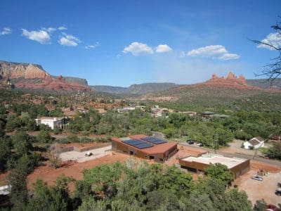 A wide view of buildings and roads, including the Sedona-Oak Creek USD District Office PV System, surrounded by trees and red rock formations under a clear blue sky in a desert landscape.