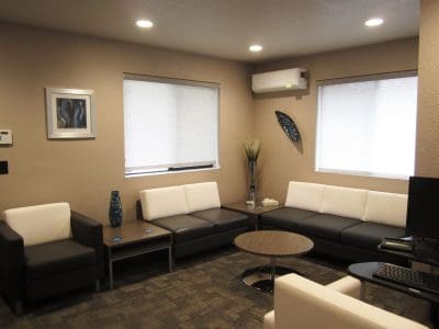 Modern office waiting room with white and dark gray sofas, a round coffee table, wall art, decorative vases, and neutral-colored walls.