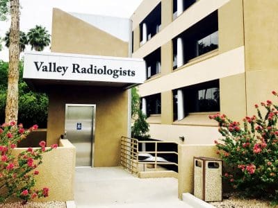 Exterior view of the Valley Radiologists building with tan walls, large windows, flowering bushes, and a ramp leading to the entrance.